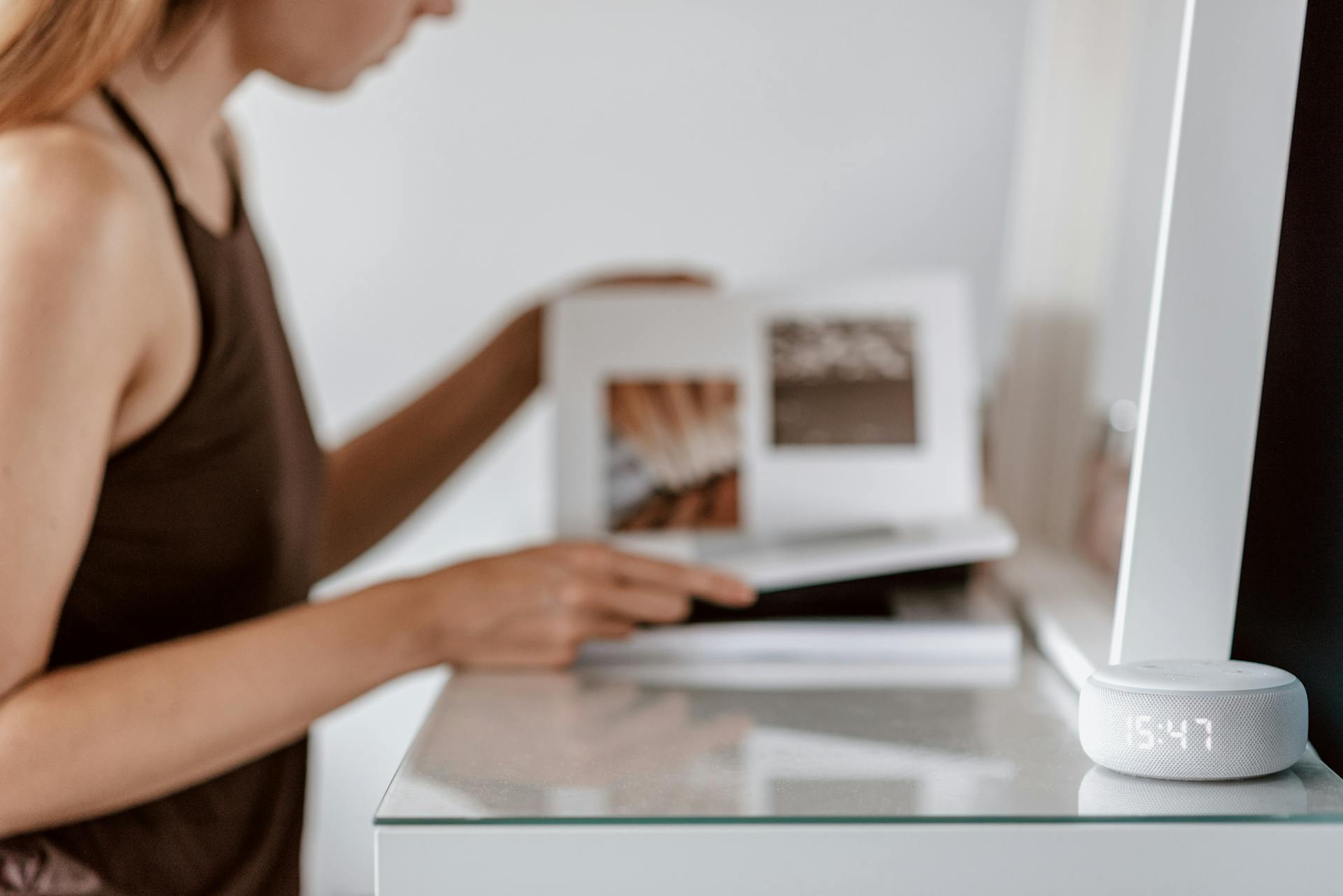 A woman reading a book with a smart speaker on a table, indicating modern tech and lifestyle.