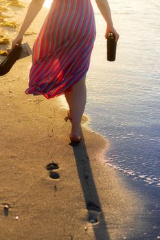 A woman in a striped dress walks barefoot on a sandy beach in Cuba during sunset.