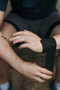 Detail of an athlete wrapping hand with black tape before training.