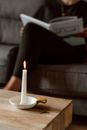 Crop anonymous female reading textbook with crossed legs on couch behind glowing candle on table at home