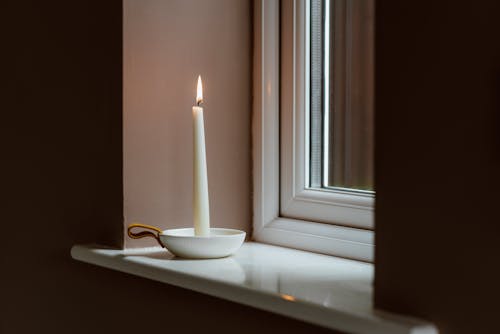 Burning candle in bowl on windowsill in evening