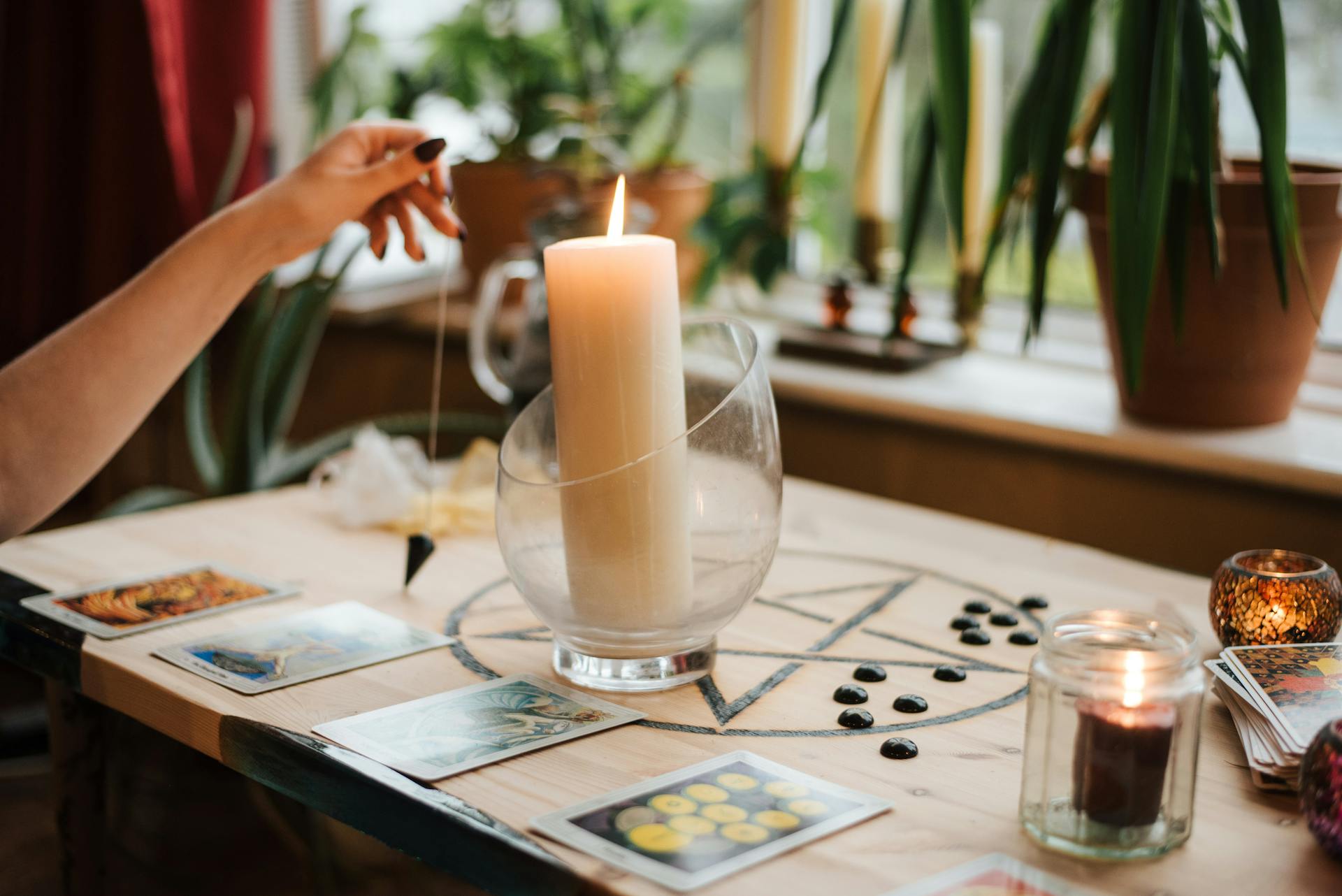 Crop unrecognizable female fortune teller with amulet near tarot cards and shiny candles during prediction process at home