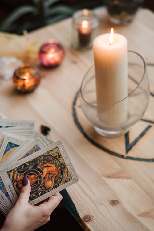 Free From above of crop anonymous fortune teller with set of tarot cards near burning candles during divination process Stock Photo