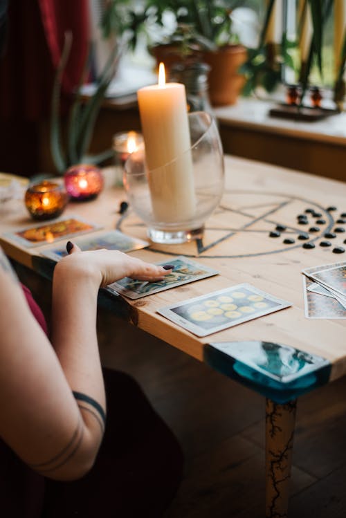 Free Crop unrecognizable female fortune teller predicting fate with tarot cards near burning candles on table at home Stock Photo