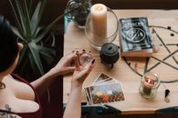 From above of crop unrecognizable female soothsayer with magic ball near tarot cards and candles during divination process in house