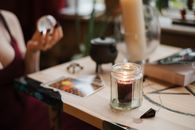 Crop anonymous female soothsayer with magic ball near shiny candle during divination process at home