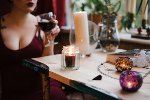 Free Crop anonymous female fortune teller with glass of potion near burning candles in house Stock Photo