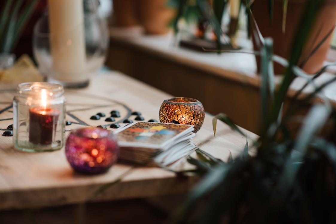 Luminous candles in holders near tarot cards on table with oracle symbol at home