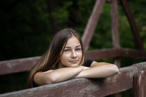 Free Teen girl with long hair standing on wooden bridge and leaning on railing while looking at camera Stock Photo