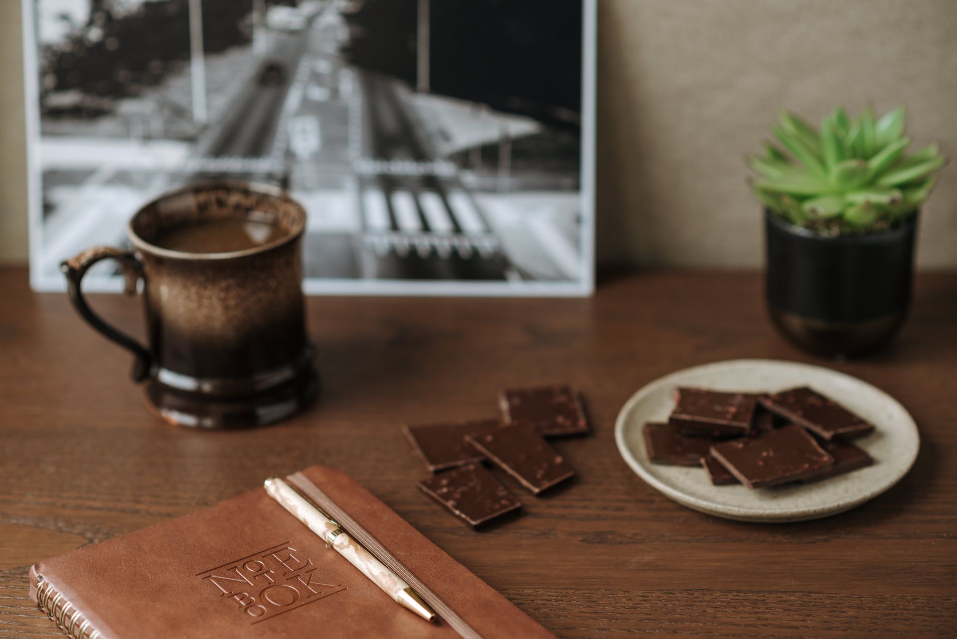 High angle of notebook with leather cover near milk chocolate and cup of fresh aromatic coffee on wooden table