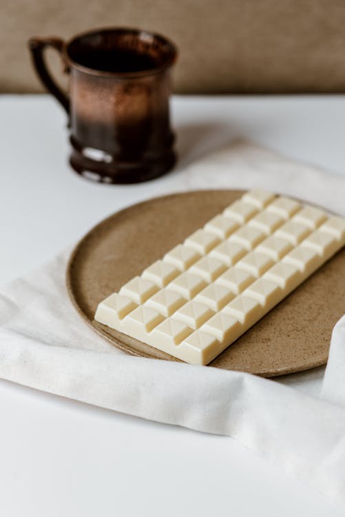 Delicious chocolate in ceramic plate on white textile near cup of coffee on table