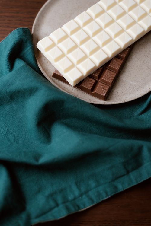 Free High angle of white and milk bars of chocolate in ceramic plate on wooden table near towel Stock Photo