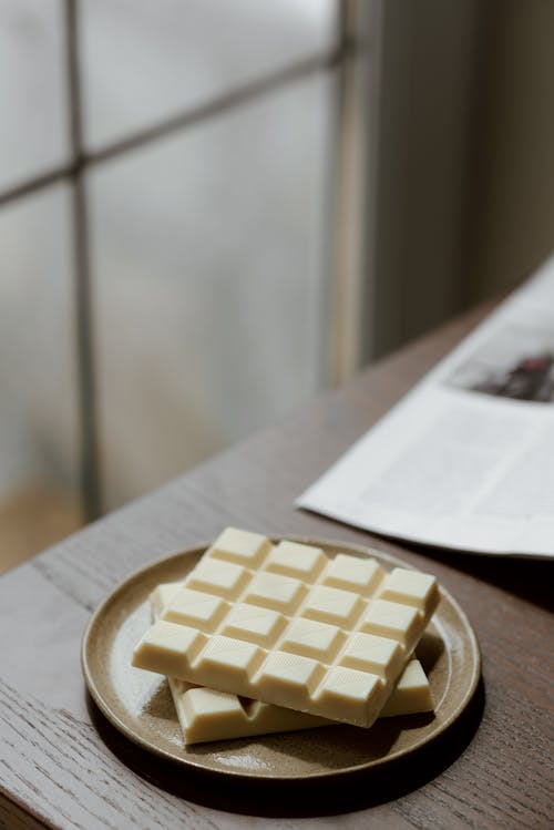 High angle of tasty white chocolate on ceramic plate near magazine on wooden table
