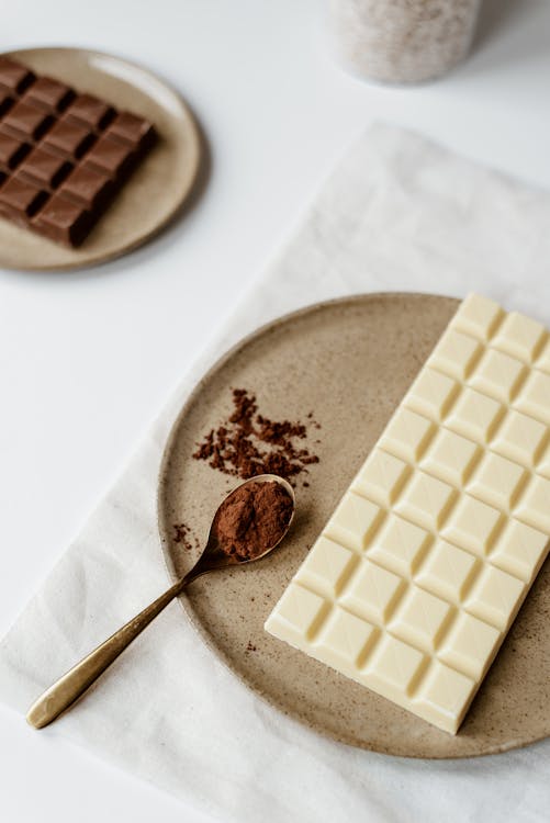 From above of delicious bar of chocolate and spoon with cacao powder on plate