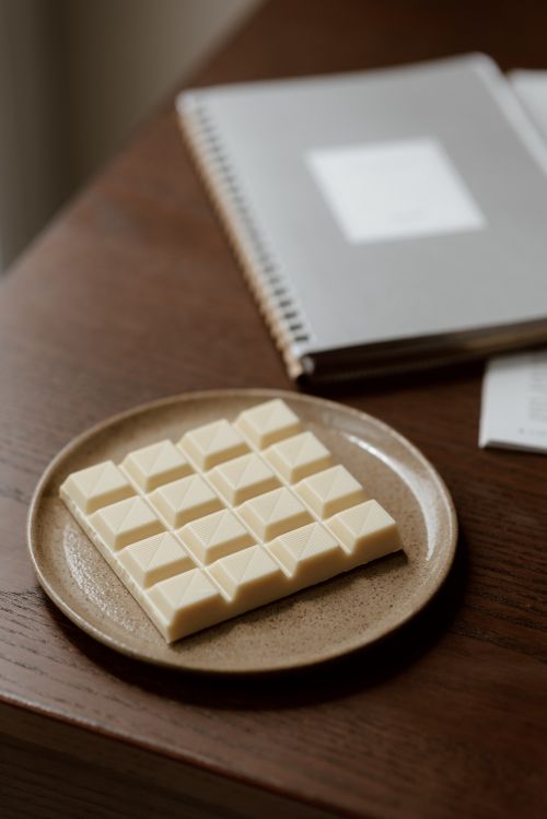 Free High angle of tasty bar of white chocolate on ceramic plate near notebook on wooden table Stock Photo