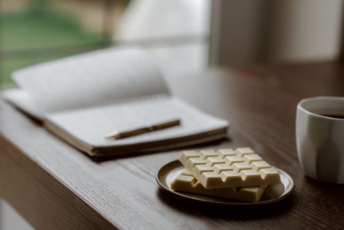 Free White chocolate on ceramic plate near opened notebook with pen and cup of coffee Stock Photo