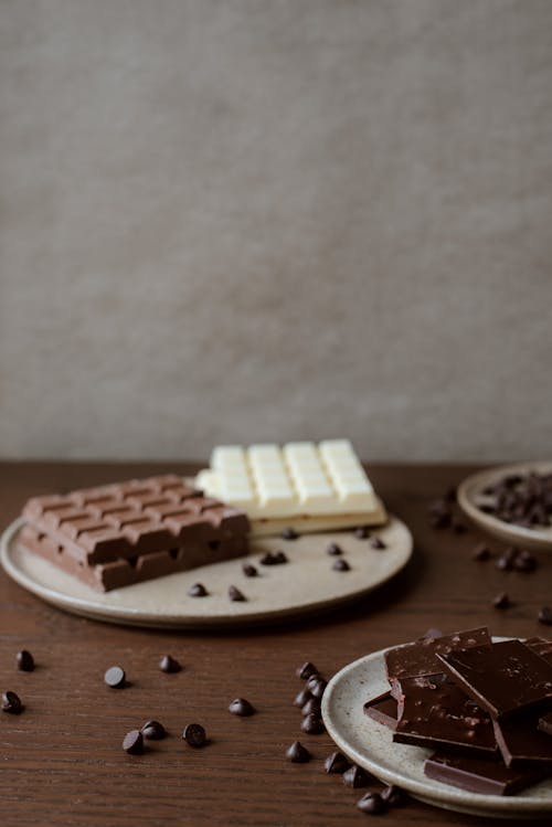 Delicious chocolate bars on ceramic plates near chocolate chips on wooden table at home