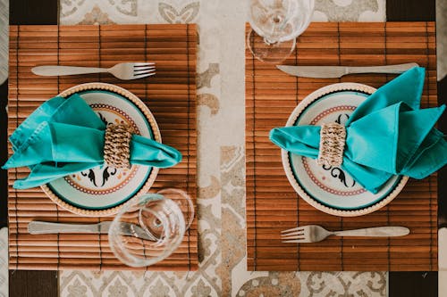 Top view stylish arrangement of ornamental plates with blue napkins served on place mat on table near wineglasses