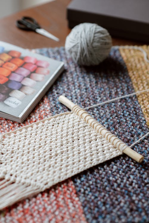 High angle of beige knitted piece near ball of yarn on table at home