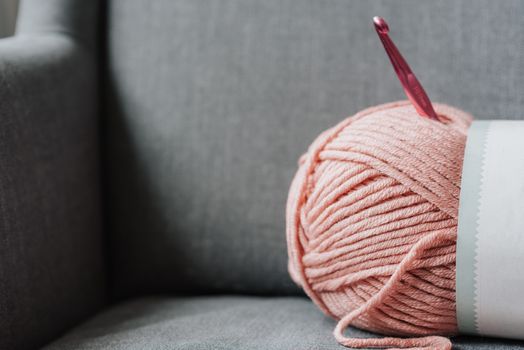 Soft pink yarn for knitting with metal crochet hook on cozy gray couch at home
