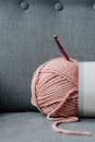 Ball of soft yarn for knitting with pink crochet hook on gray comfortable couch at home