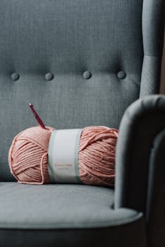 Pink yarn with hook on a blue armchair, ideal for DIY and knitting enthusiasts.