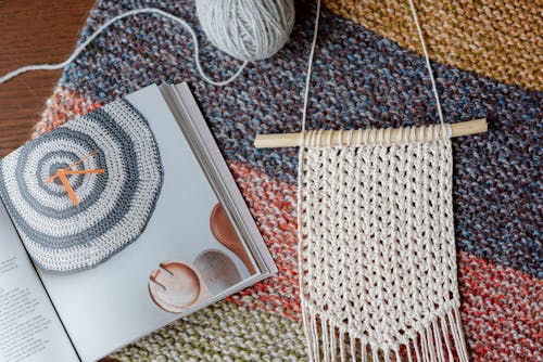 Top view of composition of white macrame decor near colorful magazine and knitting ball on table