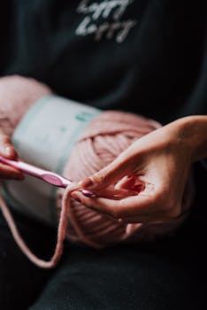 在一个舒适的室内环境中，镜头聚焦于一位女士用粉红色羊毛纱线进行钩编的手