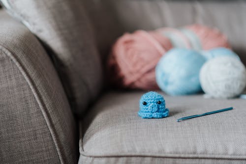 Soft blue crocheted animal toy near hook and yarns on cozy sofa at home