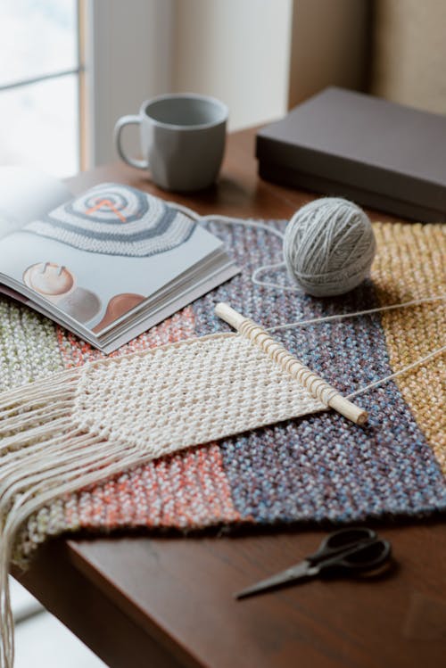 High angle of beige knitted macrame with ball near colorful magazine on wooden table