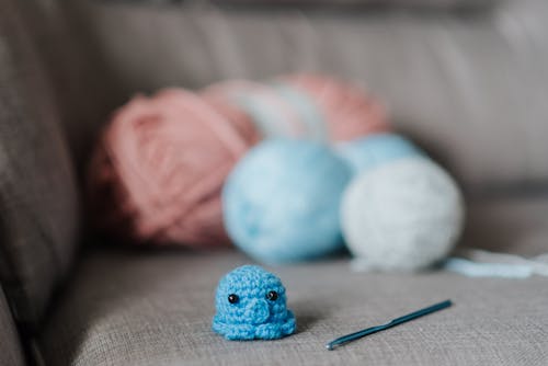 Small soft knitted animal toy with crochet hook and balls of yarn on cozy sofa