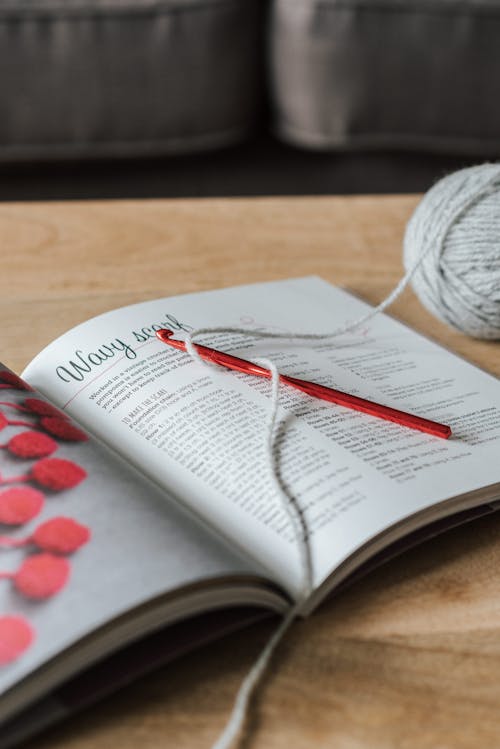 Free High angle of gray yarn ball with crochet hook and craft magazine on wooden table at home Stock Photo