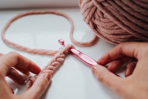 Crop woman crocheting soft pink scarf