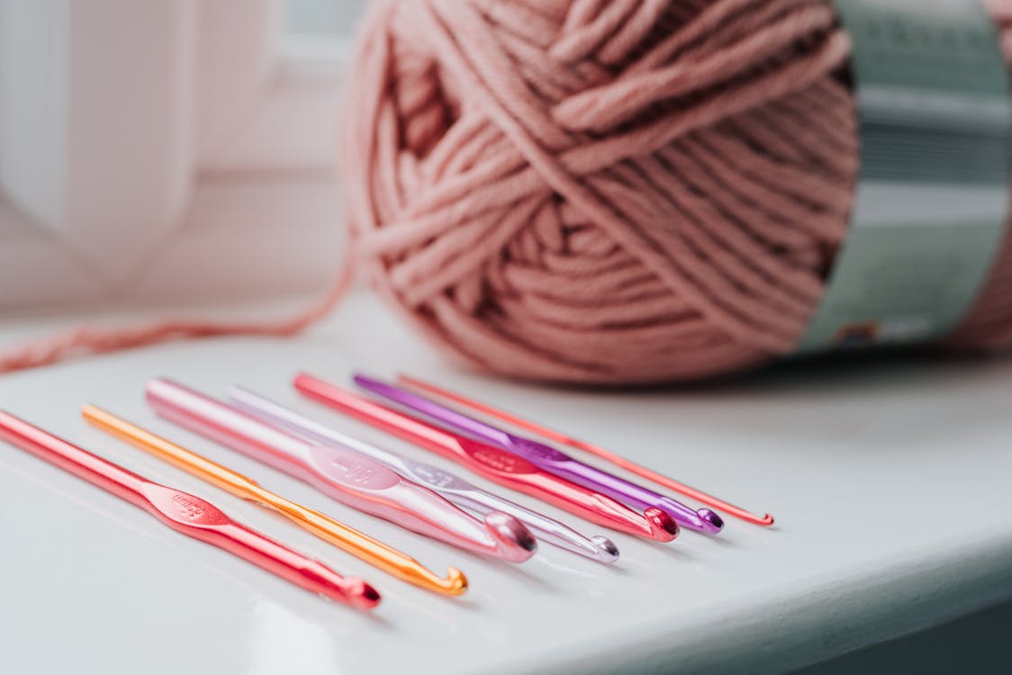 Free Closeup of row of multicolored crochet needles and ball of beige threads for knitting in bright room Stock Photo