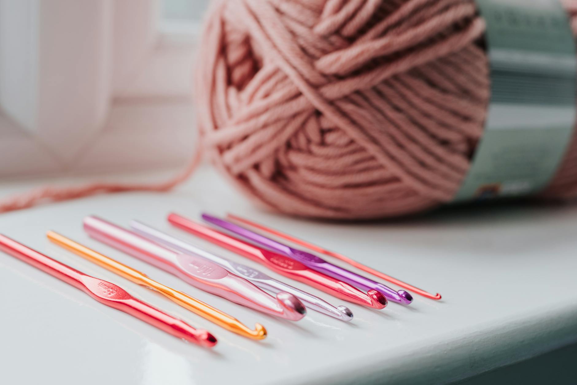 Closeup of row of multicolored crochet needles and ball of beige threads for knitting in bright room.
