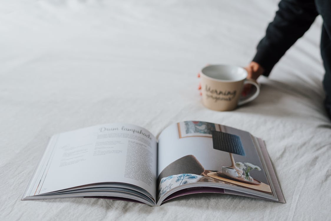Free Crop faceless person resting on bed with magazine and coffee Stock Photo