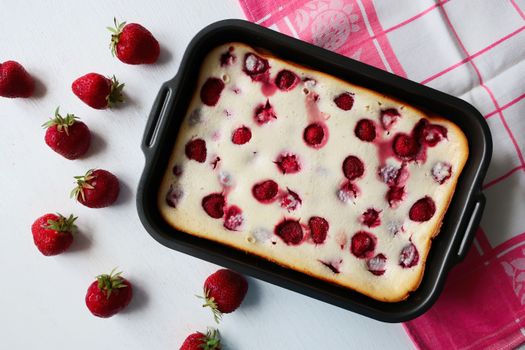 Top view of a homemade strawberry cheesecake in a baking tray, garnished with fresh strawberries.