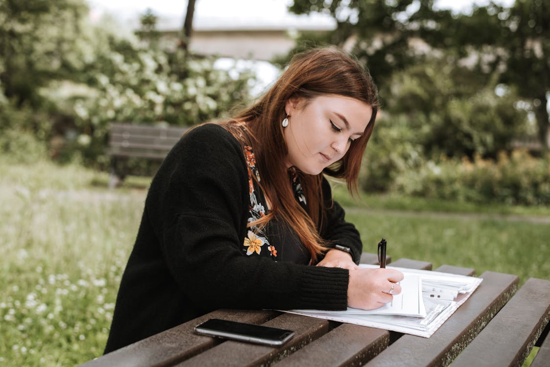 Free Concentrated woman writing notes in papers in park Stock Photo