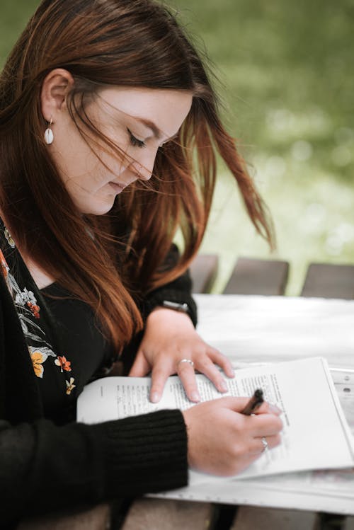 Crop woman writing notes in documents in garden