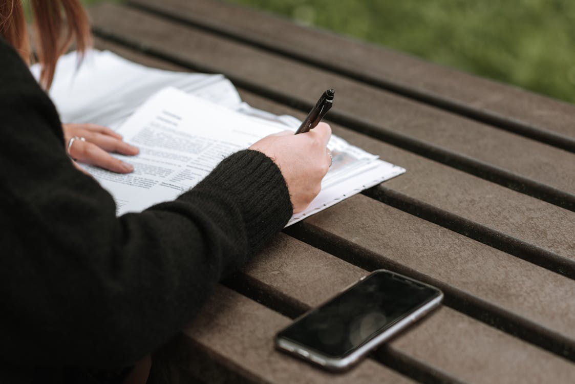 Free From above of crop anonymous female writing with pen in documents on wooden table in park Stock Photo