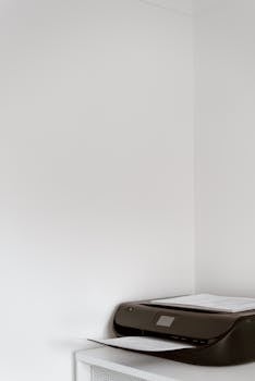 A sleek black printer in a modern office corner on a white cabinet with ample copy space.