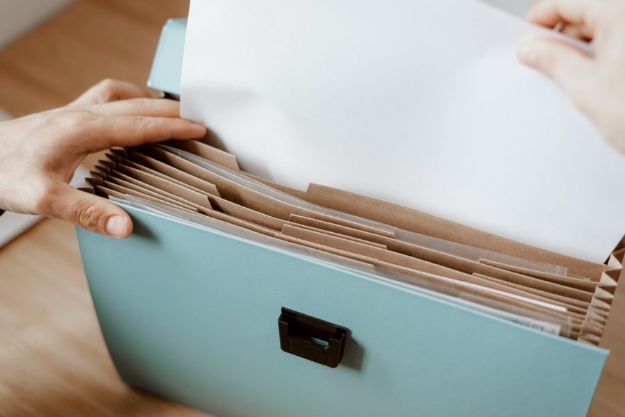 Crop faceless person putting sheet of paper in briefcase for documents placed on table