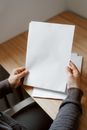 High angle of person sitting at empty wooden table and showing sheet of paper