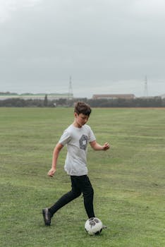 A young boy enjoying a game of soccer on a wide green field during the day.