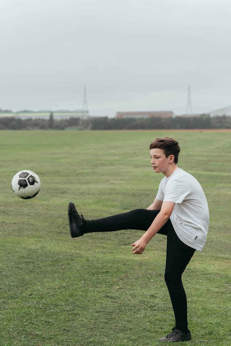 Boy Kicking Football Ball In Field