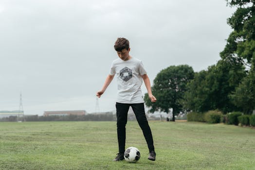 Teen boy concentrating while playing soccer on a grassy field in the park.