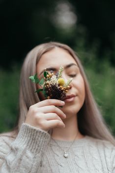 在宁静的户外环境中，一位年轻女子闭着眼睛，手捧鲜花