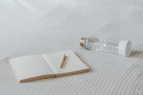 Free Open blank agenda with pen near small transparent bottle of pure water on creased bed sheet Stock Photo
