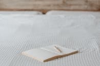 Open blank notepad with pen on creased bed sheet with ornament in light bedroom