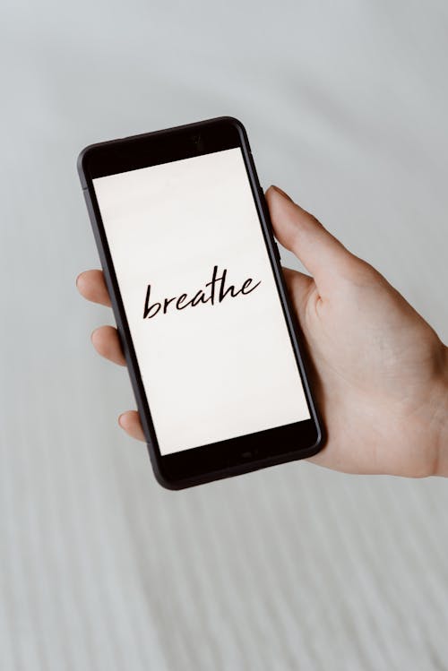 Free From above of crop unrecognizable person demonstrating cellphone with Breathe inscription above bed sheet Stock Photo